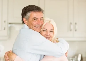 A smiling older couple embraces warmly in a bright room.