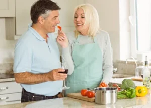 A smiling couple in a kitchen prepares a meal together