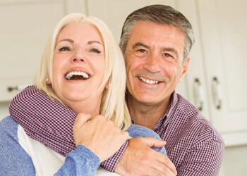 A couple embraces in a kitchen both smiling widely