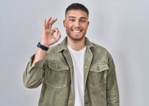 A man in a green jacket smiling, and making an "OK" hand gesture. Happy and approachable tone.