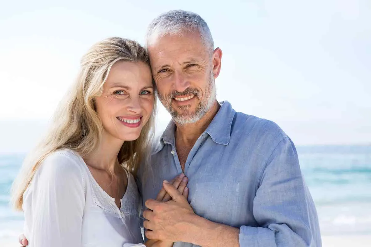 A smiling couple stands closely on a sunny beach