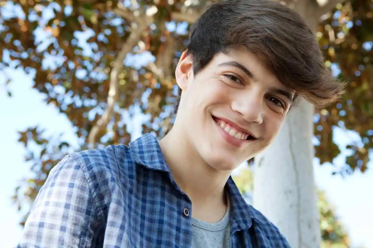 Young person standing in front of a sunlit tree.