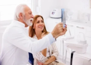 Elderly man and young woman in a dental office, smiling and examining an X-ray together.