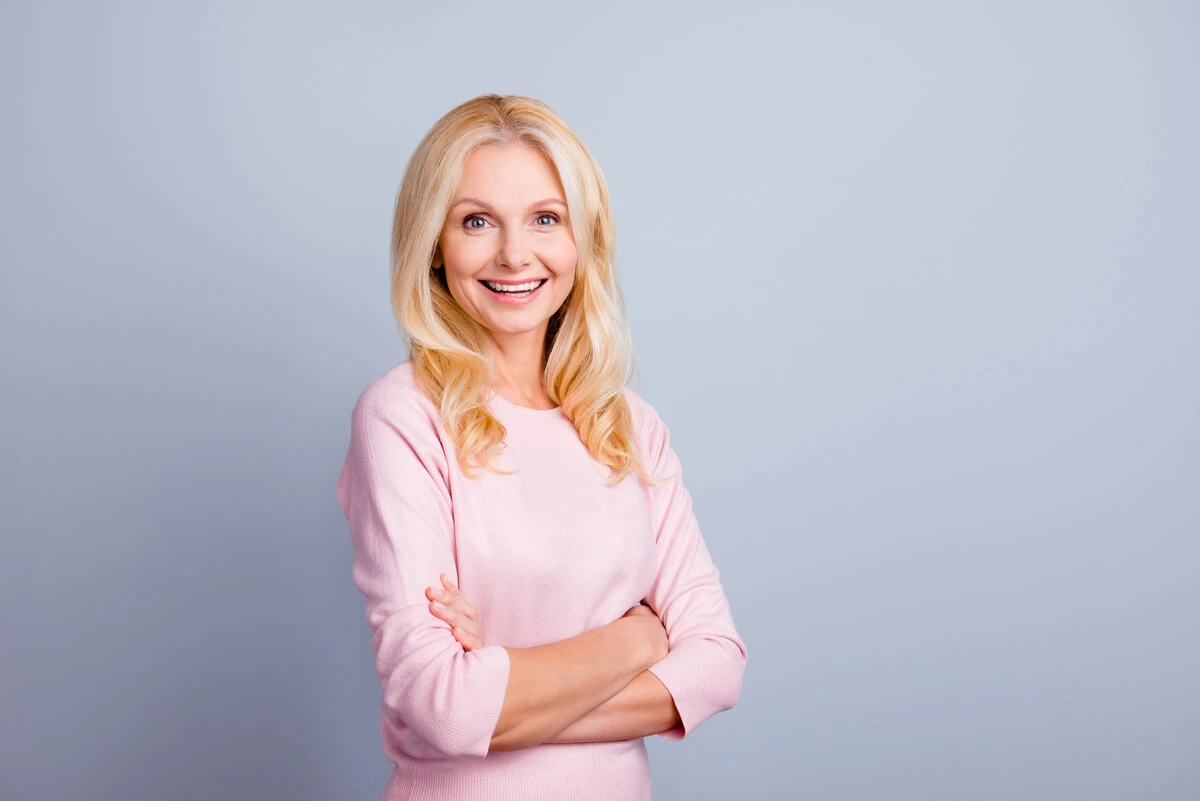 Woman arms crossed wearing a light pink sweater against a plain gray background