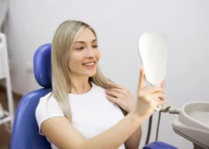 A woman with long blonde hair admiring her new smile in a hand mirror, demonstrating the effective use of veneers for crooked teeth to achieve an instantly straighter and more confident appearance.