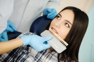 A dentist using a professional shade guide to help a young woman choose the perfect hue for her veneers, illustrating the meticulous color-matching process used to ensure natural-looking results during a dental breakdown consultation
