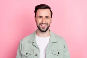 A smiling man against a pink background, showcasing a strong and healthy smile restored through effective dental treatment solutions for cracked teeth.