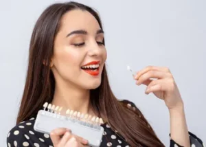 A pleased patient comparing dental shade samples to her teeth, a key step in the process explained for getting a tooth veneer to ensure a perfect, natural-looking color match