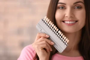 A woman holding a dental shade guide to evaluate color options, representing the technical considerations affecting the price of a cosmetic veneer, such as material quality and custom shading