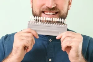 A man holding a professional tooth shade guide to his smile, demonstrating the color-matching process used by a cosmetic dentist to ensure natural-looking dental results.