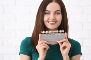 Smiling woman holds a dental shade guide, showcasing a range of tooth colors