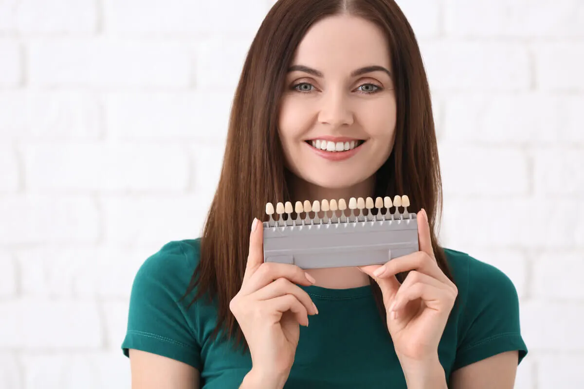 Smiling woman holds a dental shade guide, showcasing a range of tooth colors
