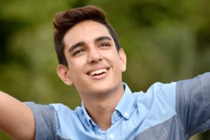 A young man smiling joyfully with his arms raised in a natural outdoor setting, celebrating the total relief from toothache pain and the freedom of a restored, healthy smile.
