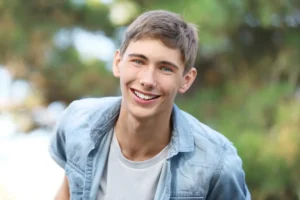 A smiling young man outdoors against a lush green background, showcasing the seamless, natural-looking results of a smile makeover using composite veneers.