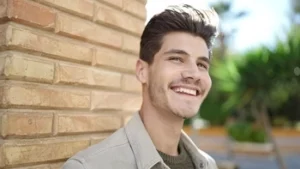 A young man with a healthy, bright smile outdoors, illustrating the long-term success of proper maintenance and care for veneers to keep them looking natural and radiant over time.