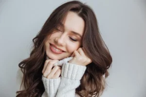 A smiling woman in a cozy white sweater with her eyes closed, radiating the comfort and confidence of a pain-free, healthy smile after restorative dental treatment