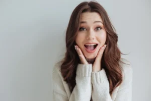 A woman expressing surprise with wide eyes and a bright smile, highlighting the dramatic 'before and after' results of a professional smile makeover or teeth whitening treatment.