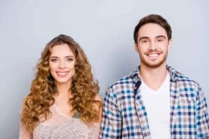 A smiling man and woman against a plain gray background, showcasing bright, healthy smiles that reflect the quality of professional preventative dental care