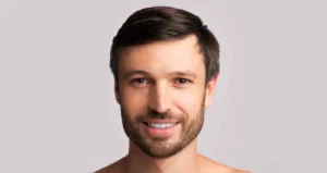 A smiling man with a neat beard and short dark hair, showcasing a healthy and confident smile that reflects the success of routine dental care