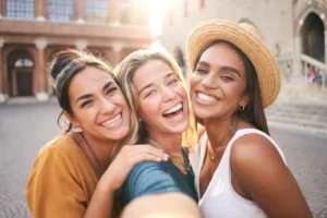 A group of three friends smiling widely for a selfie outdoors, showcasing healthy, confident smiles and the social freedom that comes from professional dental care and maintenance