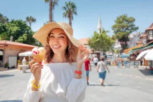A smiling woman enjoying an ice cream cone on a sunny street, showcasing a healthy, sensitivity-free smile during a vacation with palm trees.