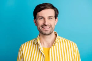 A smiling man standing against a vibrant blue background, showcasing a bright, healthy smile that reflects the success and satisfaction of regular dental maintenance