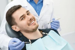 A relaxed man in a dental chair wearing a protective bib smiles during a checkup, as a professional dentist in gloves holds dental tools, illustrating a comfortable and anxiety-free patient experience