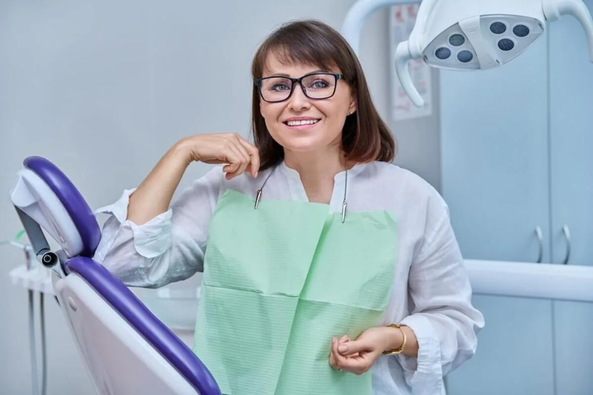 A confident woman standing in a modern dental office next to a treatment chair, portraying the peace of mind and empowerment that comes with professional dental care