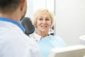 A smiling elderly woman with blonde hair looking trustingly at her dentist during an appointment, highlighting a compassionate and comfortable geriatric dental care experience