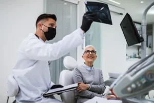 A friendly dentist discussing a digital panoramic X-ray with an older female patient, demonstrating clear communication and personalized care during a dental consultation