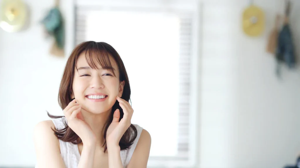 A smiling woman with brown hair resting her hands on her cheeks, radiating confidence and joy following a successful dental makeover