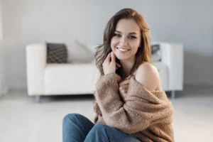 A smiling woman sitting comfortably on the floor in a bright, cozy room, reflecting the confidence and happiness that comes with a healthy dental smile
