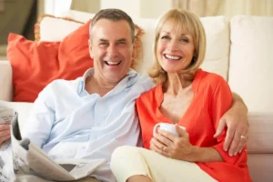 A smiling couple enjoying a relaxed morning on a couch, representing the confidence and comfort of a healthy, beautiful smile after dental treatment.