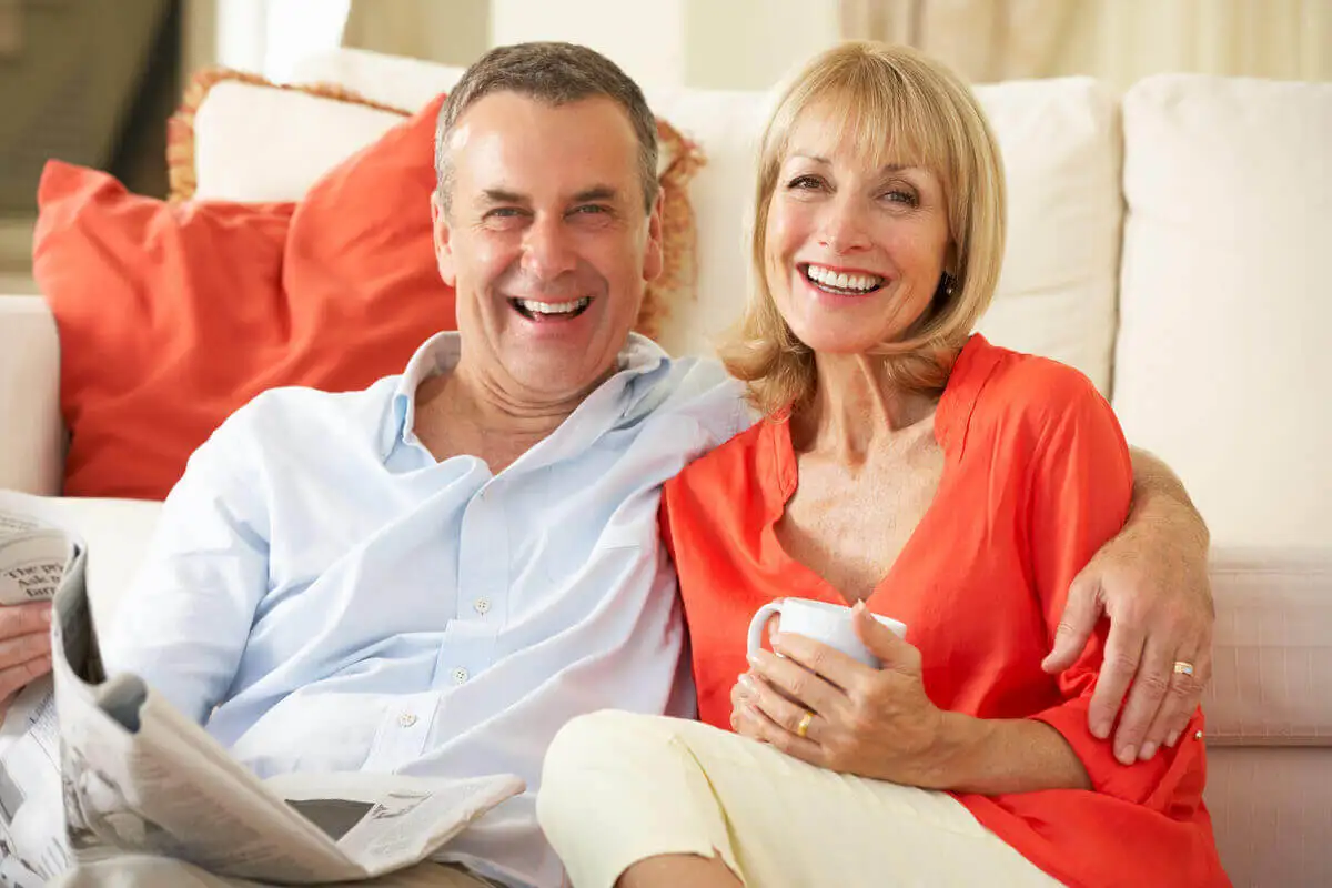 A smiling couple enjoying a relaxed morning on a couch, representing the confidence and comfort of a healthy, beautiful smile after dental treatment.