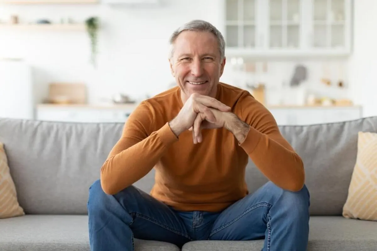 A smiling man sitting comfortably on a modern gray sofa, representing a relaxed and positive patient experience at a dental clinic