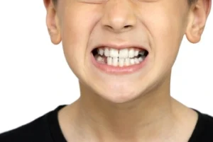 A child in a black shirt grits their teeth, displaying a tense expression with eyes squinted