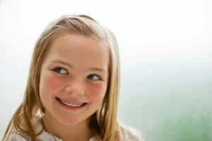 Smiling girl with blonde hair and braces looking to the side, wearing a white shirt