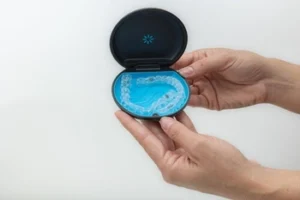 Hands holding an open black case with a blue interior, showcasing a clear dental aligner
