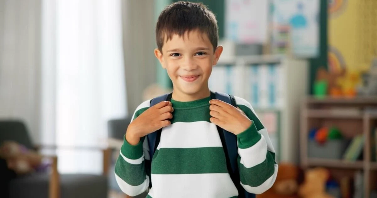 Young boy smiling confidently, wearing a green and white striped sweater and backpack