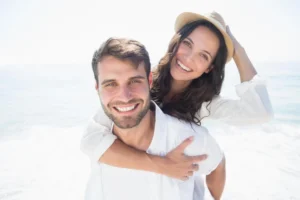 A cheerful couple by the sea, with the woman playfully giving the man a piggyback ride