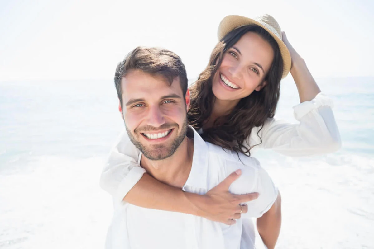 A cheerful couple by the sea, with the woman playfully giving the man a piggyback ride