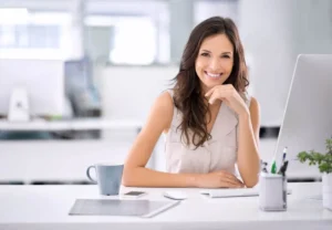 A smiling woman sitting at a bright office desk, showcasing a radiant and confident smile