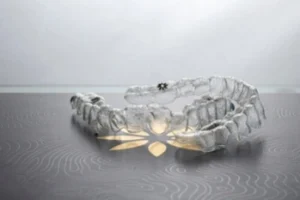 How Does Invisalign Work set A translucent, serpentine sculpture resembling a segmented spine is displayed on a wavy-patterned surface