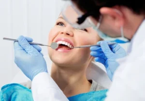 Teeth Whitening Bali consult Smiling patient at a dental check-up. Dentist wears gloves, using a mirror and probe to examine her teeth