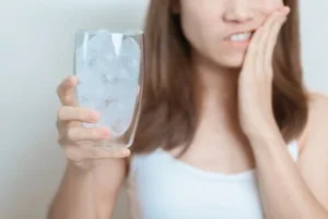 Tooth Cavity Pain sensitivity A woman holds a glass filled with ice, her expression pained as she touches her cheek, suggesting tooth sensitivity or discomfort