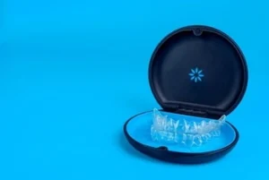 Black,Plastic,Case,With,Transparent,Braces,On,Blue,Background.,Insivible A clear dental aligner sits in an open black case