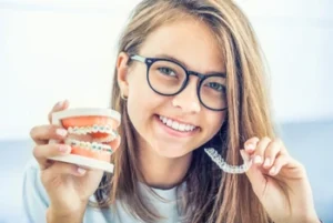 Dental,Invisible,Braces,Or,Silicone,Trainer,In,The,Hands,Of Smiling girl holds dental model with braces in one hand and a clear aligner in the other, conveying a theme of orthodontic care