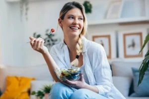 A woman enjoys a fresh salad, maintaining a healthy smile