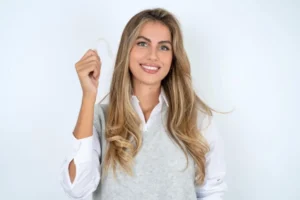 Woman smiling while holding a transparent orthodontic aligner