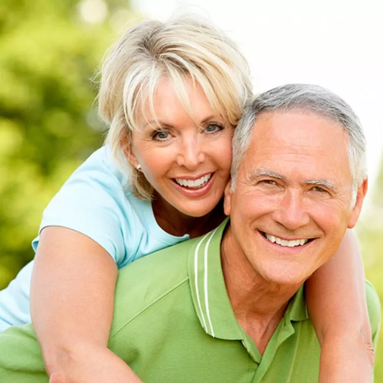 Smiling couple in a sunny park, woman playfully embracing the man from behind